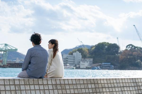 堤防に腰掛ける若い夫婦、将来を話し合っているイメージ
